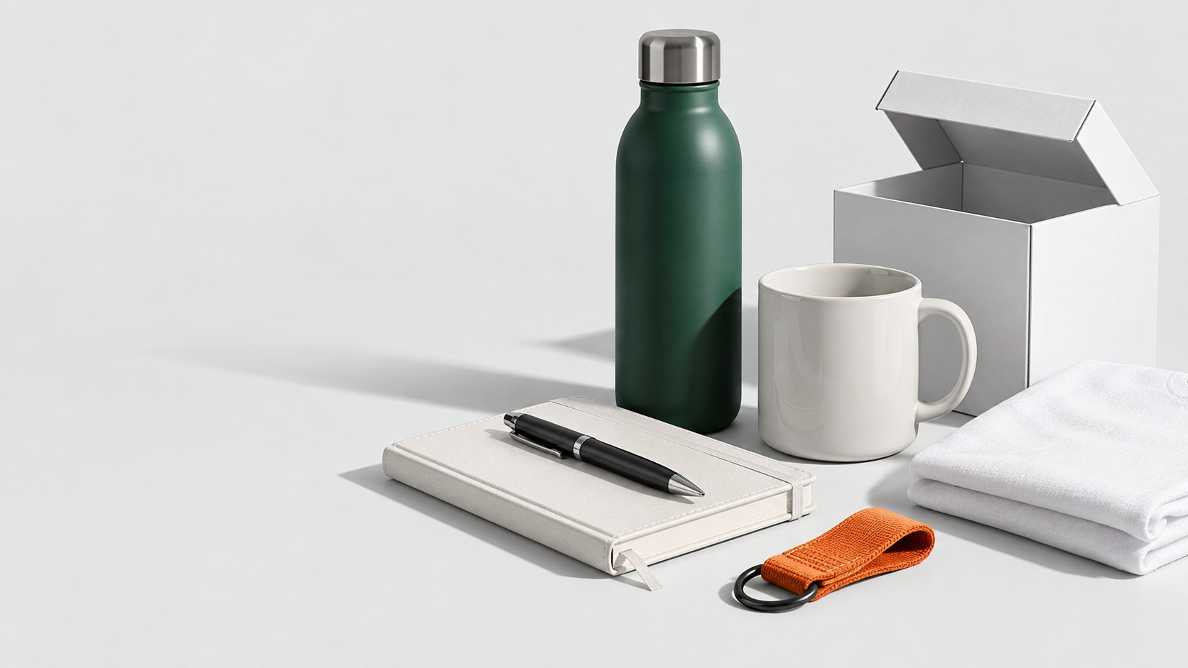 Studioaufnahme verschiedener Werbeartikel: Trinkflasche, Tasse, Notizbuch, Textil, Schlüsselanhänger und Geschenkkarton